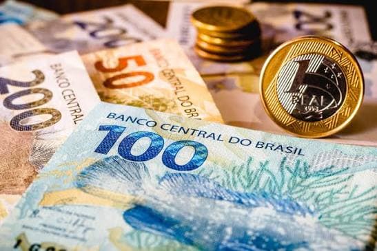 Notas e moedas de real representando o limite de faturamento e impostos do MEI em 2026